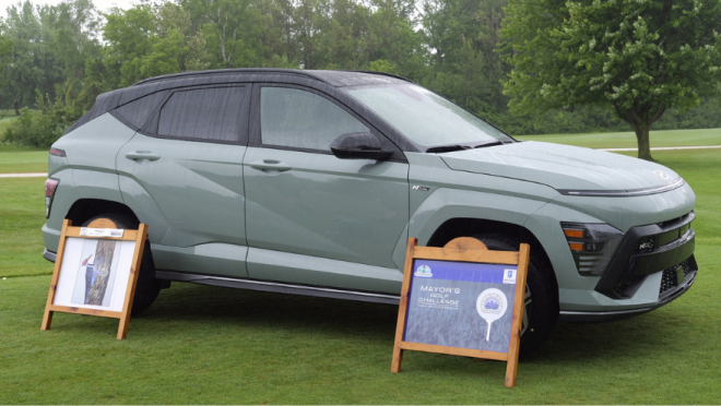 A light green SUV is parked on a golf course with two wooden A-frame signs next to it.