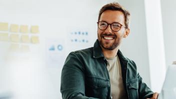 Man with glasses looking to the side and smiling.