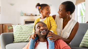 Family unit consisting of a father, mother and a daughter smiling at each other.