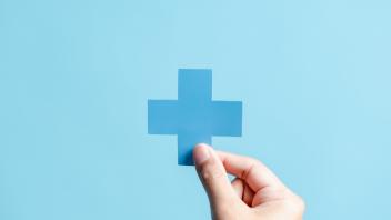 Hand holding a blue cross. The background is a lighter shade of blue.