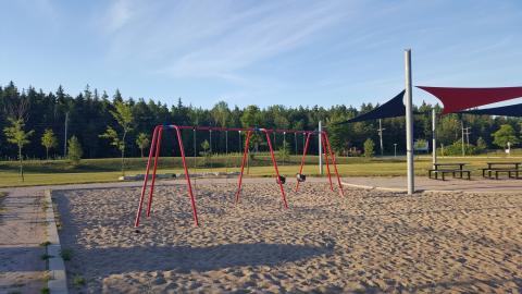 Mair Mills Swing Set Two child and two toddler swings. Concrete area with shade sails and picnic tables.