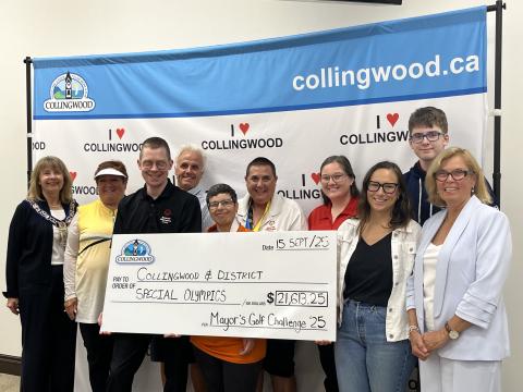 A group of people stand holding a giant cheque