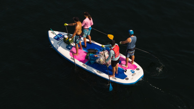 4 people on a stand up paddle board with garbage they collected