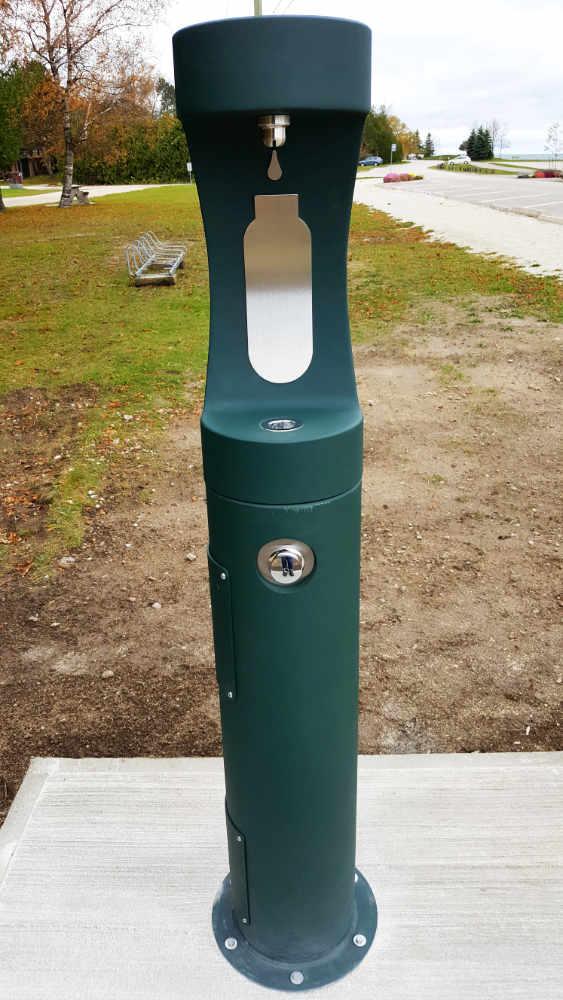 A tall, narrow and dark green water fountain in a park